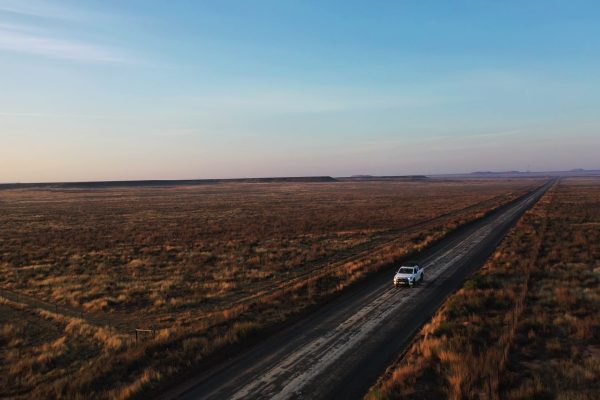 a lone car driving on a straight road through a barren landscape