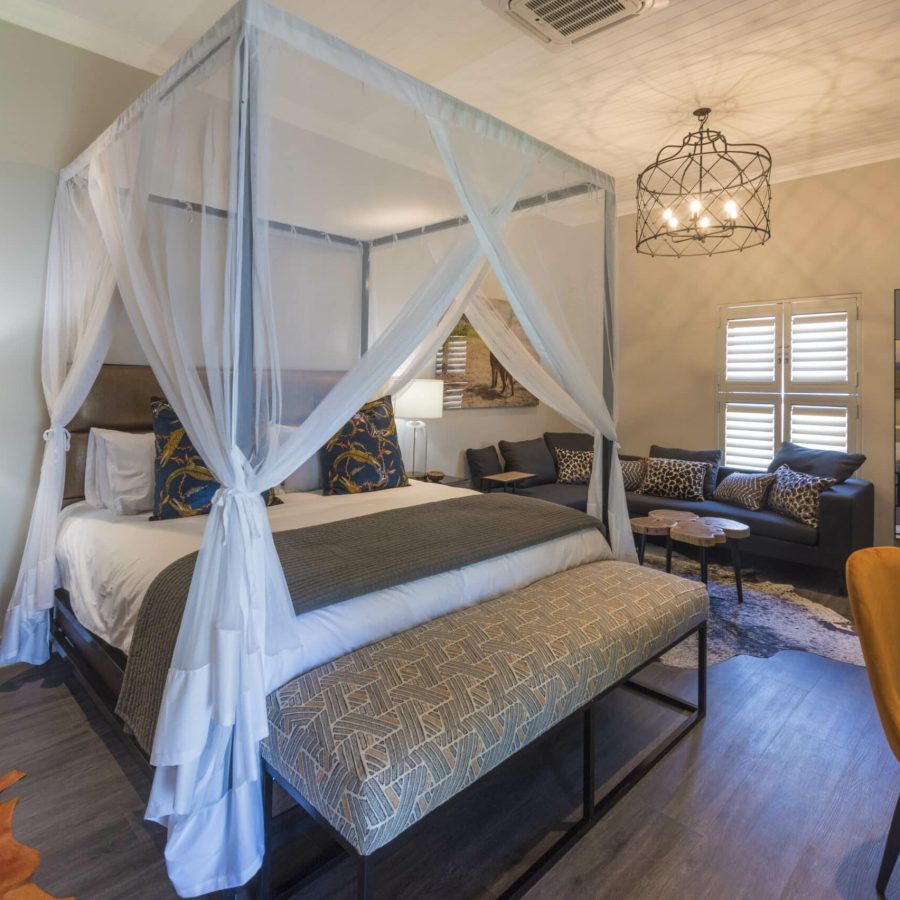 a beautifully decorated room with an african theme, large 4-poster king size bed draped mosquito netting, lounge area and desk