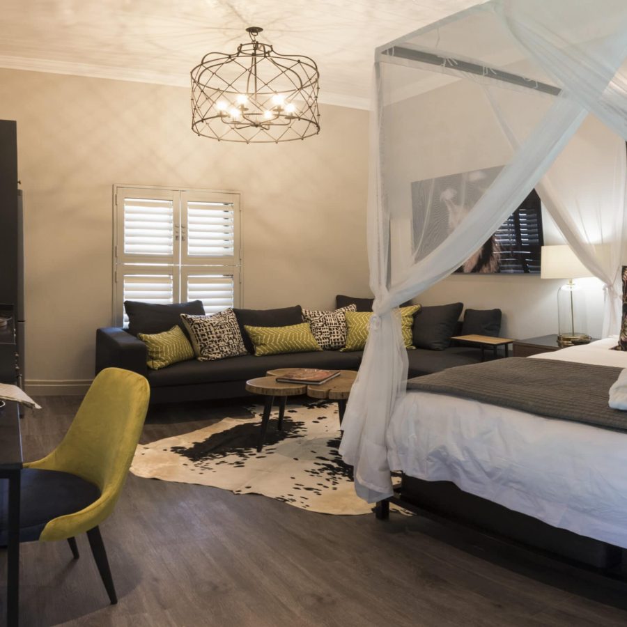 a beautifully decorated room with an african theme, large 4-poster king size bed draped mosquito netting, lounge area and desk